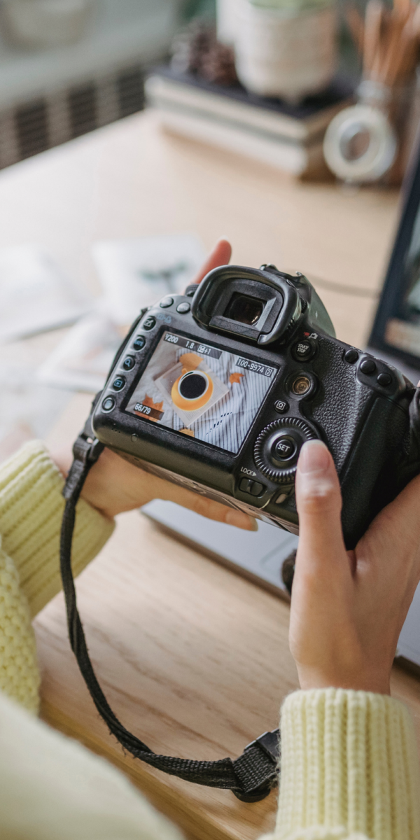A person in a yellow sweater holds a DSLR camera.